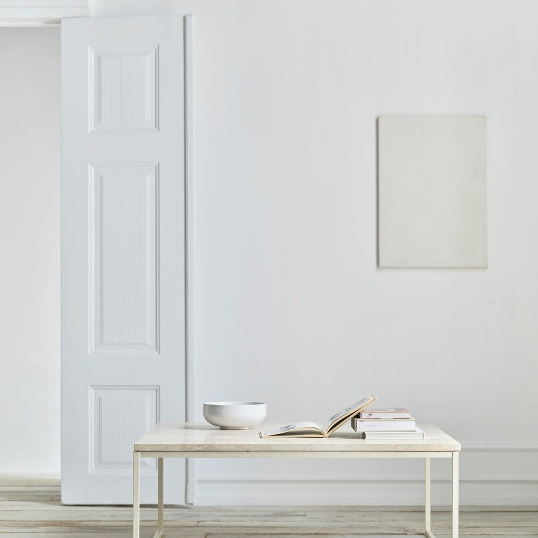 Light grey wall with a minimalistic white table, featuring a simple bowl and books, creating a serene, modern aesthetic.