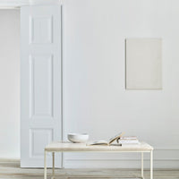 Minimalist white table with a neutral palette, featuring a plain white bowl and stacked books on a light wood floor.