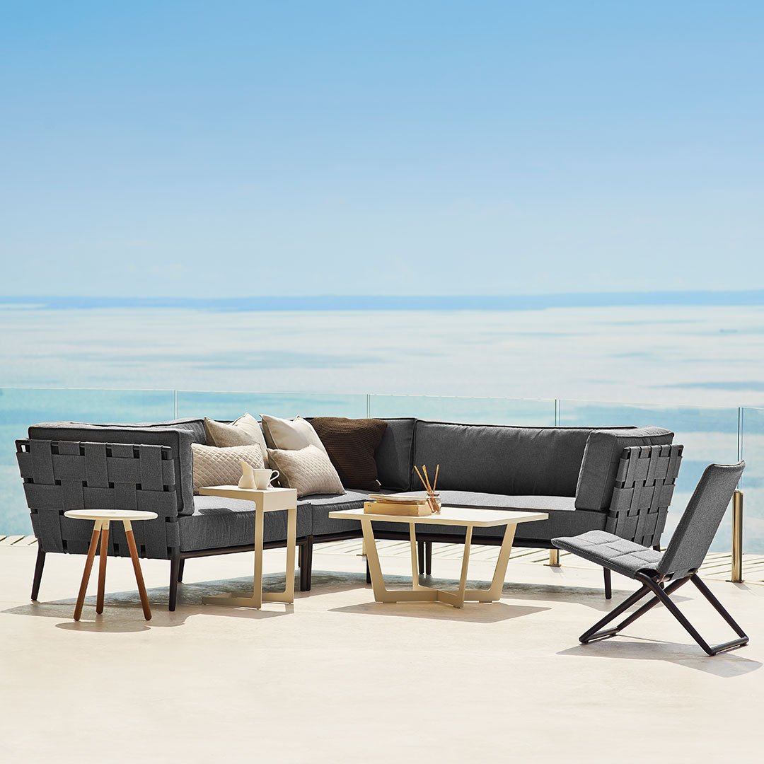 Modern outdoor sectional sofa in dark gray with cream and brown accents, featuring minimalist design and wooden tables.
