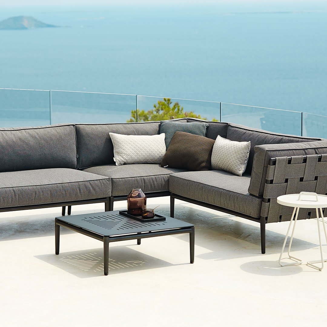 Modern gray outdoor sectional sofa with textured cushions and a sleek black metal frame, set against a serene backdrop.