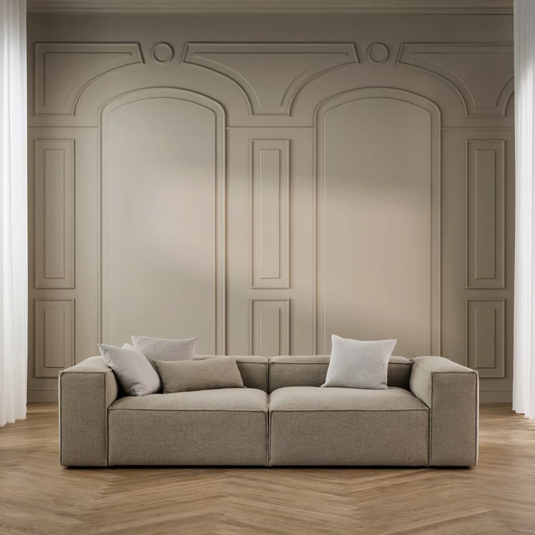 Neutral beige sofa with clean lines, paired with soft light-colored cushions against a minimalist backdrop.