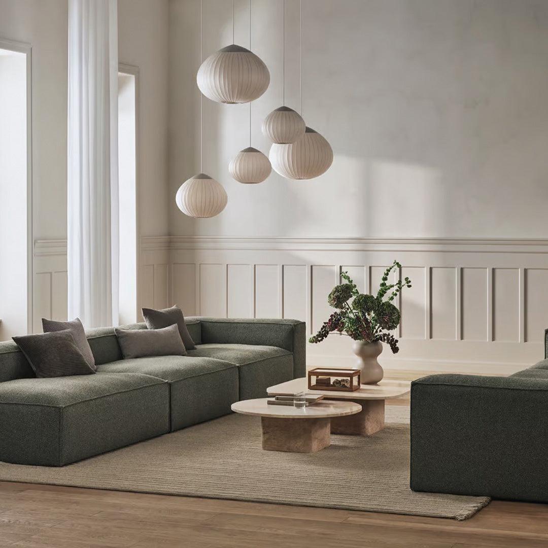 Modern living room featuring muted green sofas, neutral-toned decor, and soft textures against a light beige backdrop.