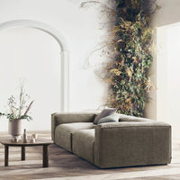 Soft olive green fabric sofa with minimalistic design, set against a neutral backdrop and natural foliage elements.