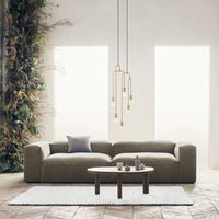 Gray textured sofa with a white area rug, complemented by gold accent lighting and lush green plants.