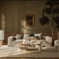 Beige and cream sofa with accent pillows in soft gray and white, set against muted textured walls, paired with round stone tables.