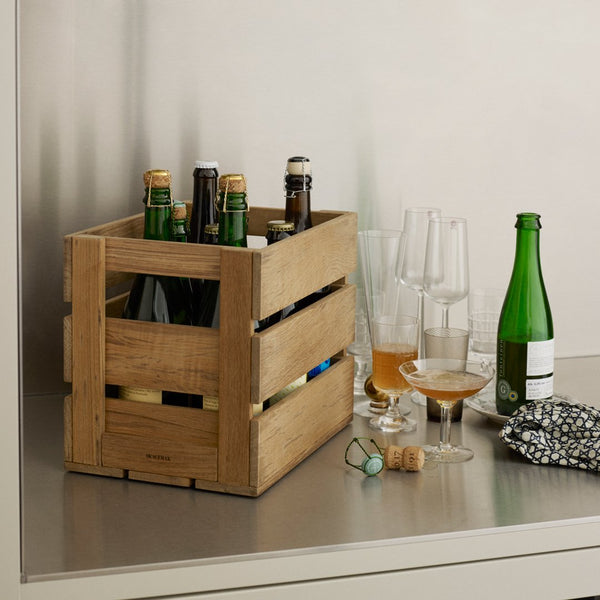 Wooden crate in a natural finish, featuring slatted design, holding assorted bottles, surrounded by various glassware.