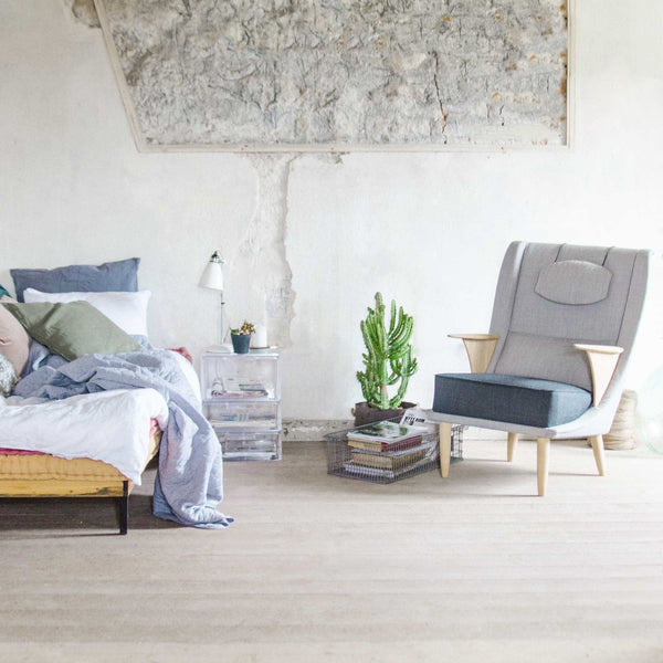 Cozy bedroom scene featuring grey, blue, and pastel tones with a textured wall and modern chair. Earthy, minimalist vibe.
