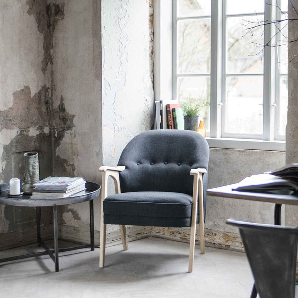 Gray upholstered chair with button tufting and light wooden arms, set against a textured wall and minimalist decor.