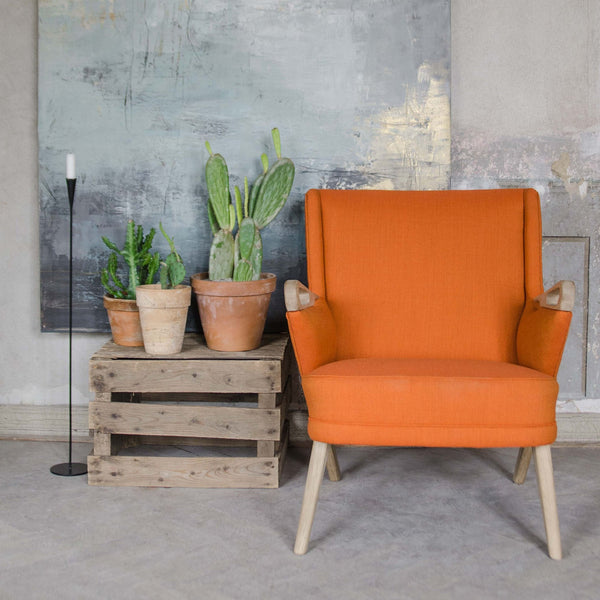 Bright orange armchair with a smooth fabric finish, set against a textured gray wall and rustic wooden crates.