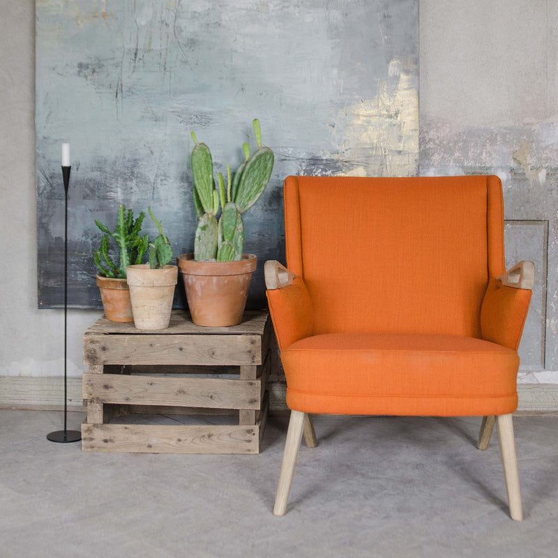 Bright orange armchair with a smooth fabric finish, set against a textured gray wall and rustic wooden crates.
