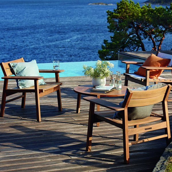 "Wooden patio chairs with blue and green cushions, accented by terracotta pillows, on a deck overlooking the water."