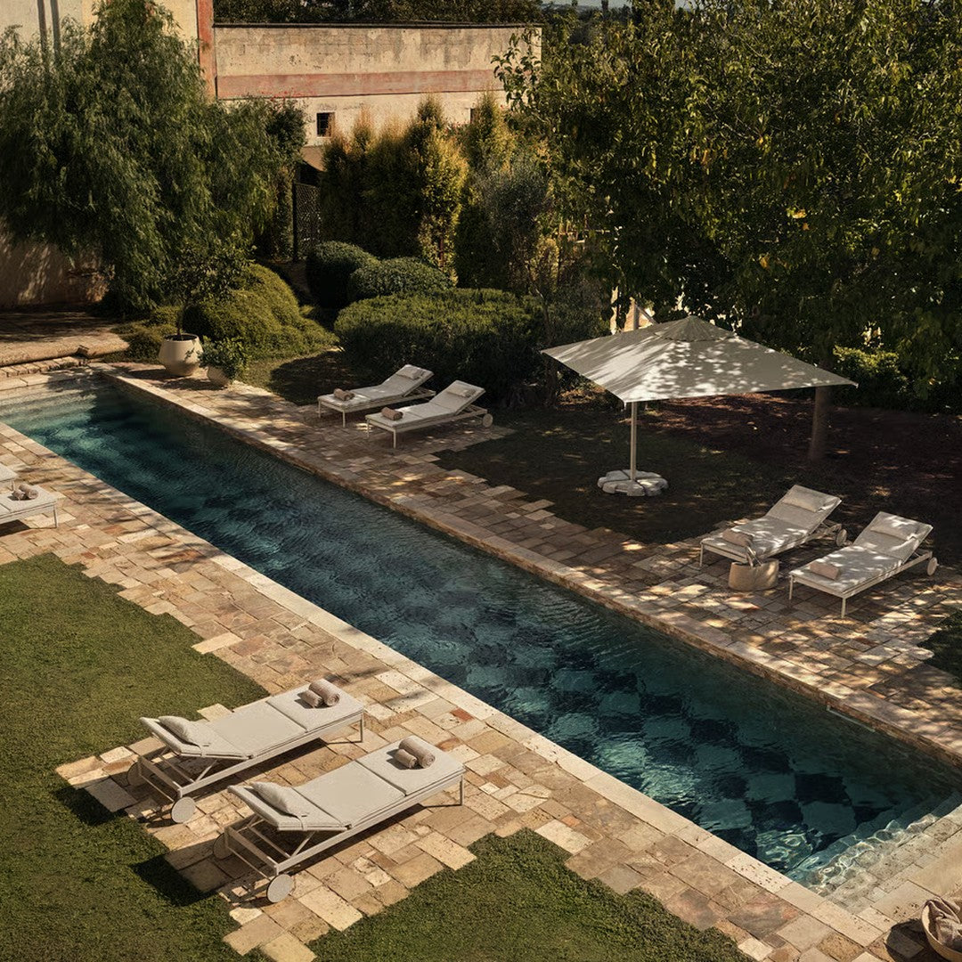 "Neutral-toned lounge chairs by a teal pool, featuring patterned tiles and lush green landscaping."