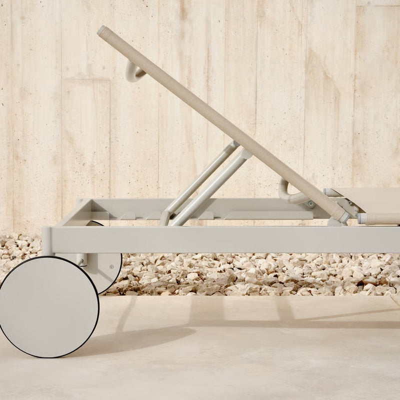 Grey chaise lounge with a minimalist design and a neutral fabric, complemented by round white wheels.