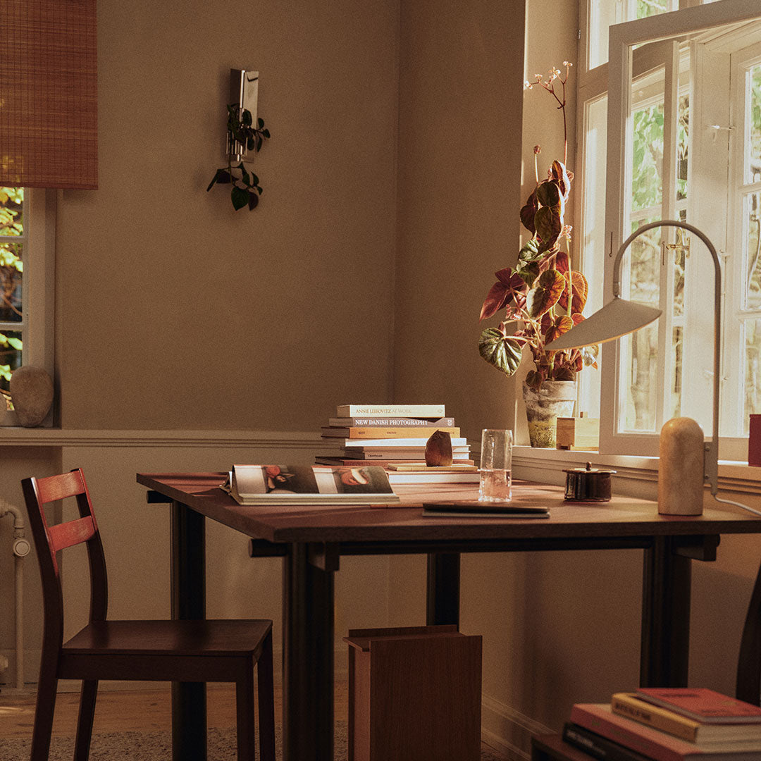 Warm beige walls, dark wooden table, and rich brown chair create a cozy, inviting workspace. Natural light adds warmth.