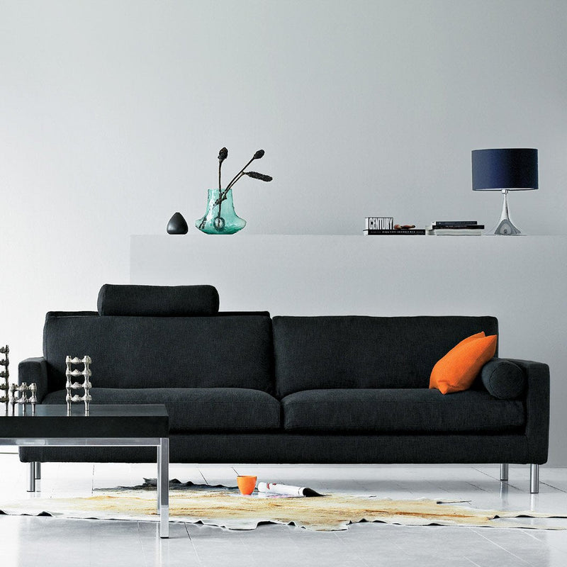 Modern black sofa with orange accent pillow, paired with a sleek glass coffee table and colorful decor elements.