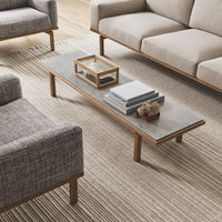 "Light grey coffee table with a smooth marble top and wooden legs, surrounded by neutral-toned sofas and a textured rug."