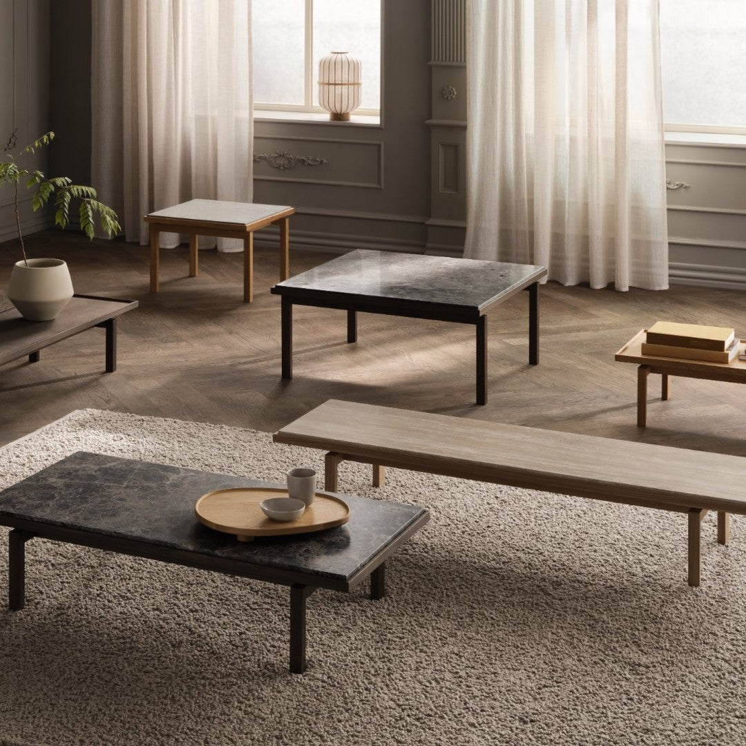 "Wood and marble coffee tables in neutral tones and varied finishes arranged on a textured light rug."
