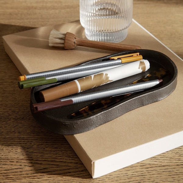 "Colorful pens in a dark tray with a tortoise shell pattern on a neutral background. Modern, minimalistic style."