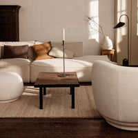 Light beige sofa with brown accents, minimalist wooden coffee table, and soft, round white pouf on a textured beige rug.