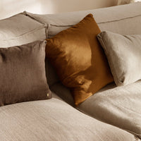 "Plush linen pillows in warm brown and mustard yellow on a soft beige sofa, featuring subtle textures."