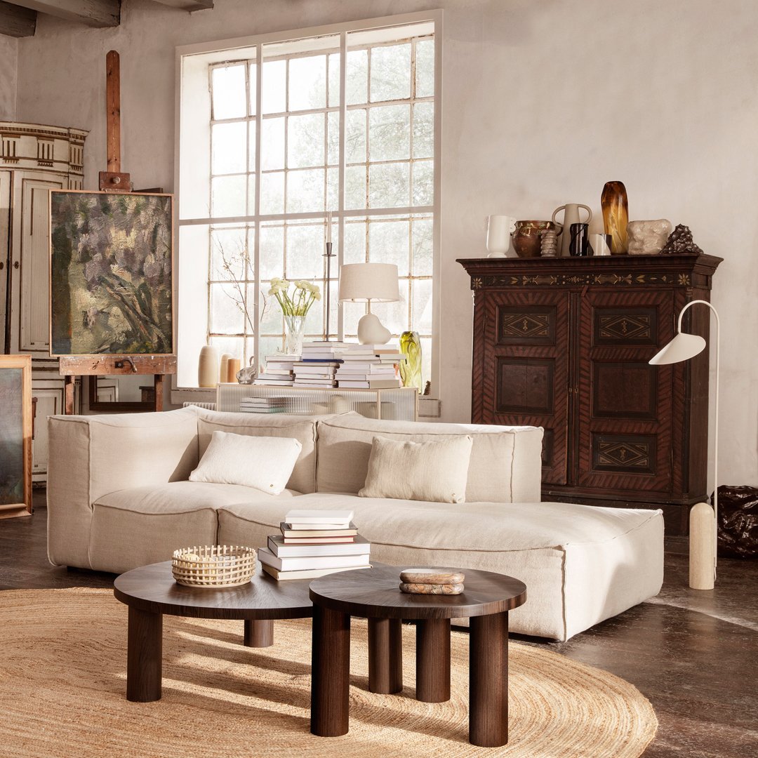 "Neutral beige sectional sofa with textured fabric and soft cushions, complemented by dark wood accents and round tables."