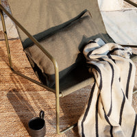 Olive green chair with striped black and white blanket, featuring a textured pattern on a natural woven rug.