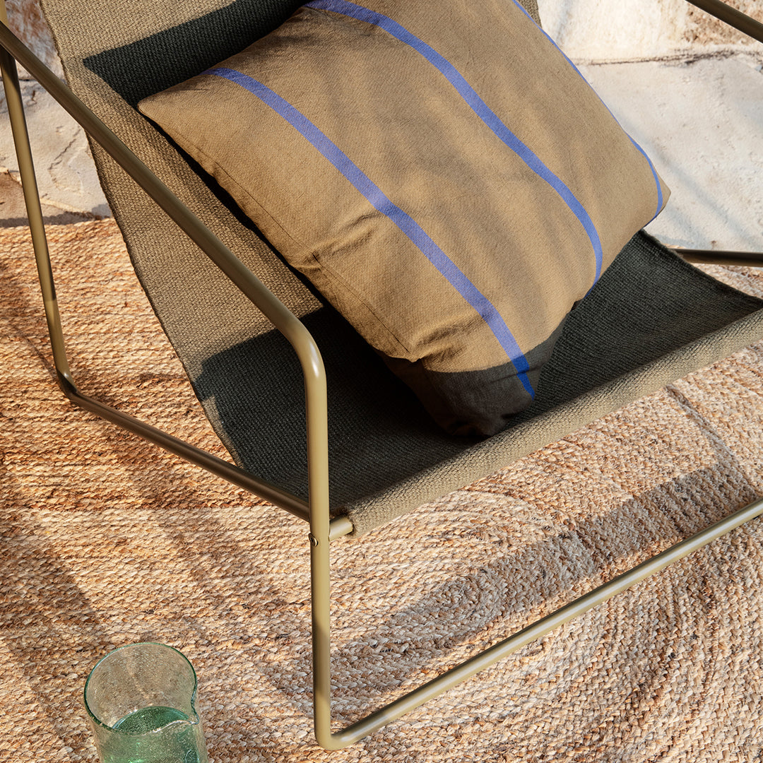 Brown and blue striped cushion on a modern chair with a textured gray fabric, set against a natural woven rug.