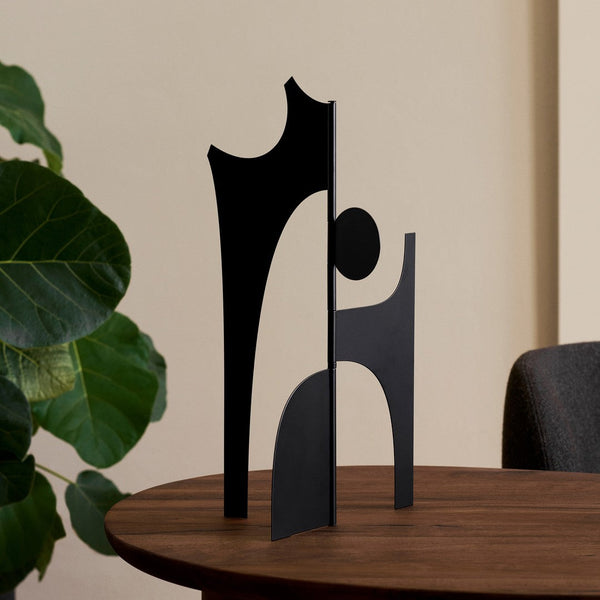 Abstract black metal sculpture with geometric shapes on a wooden table, creating a modern artistic vibe.