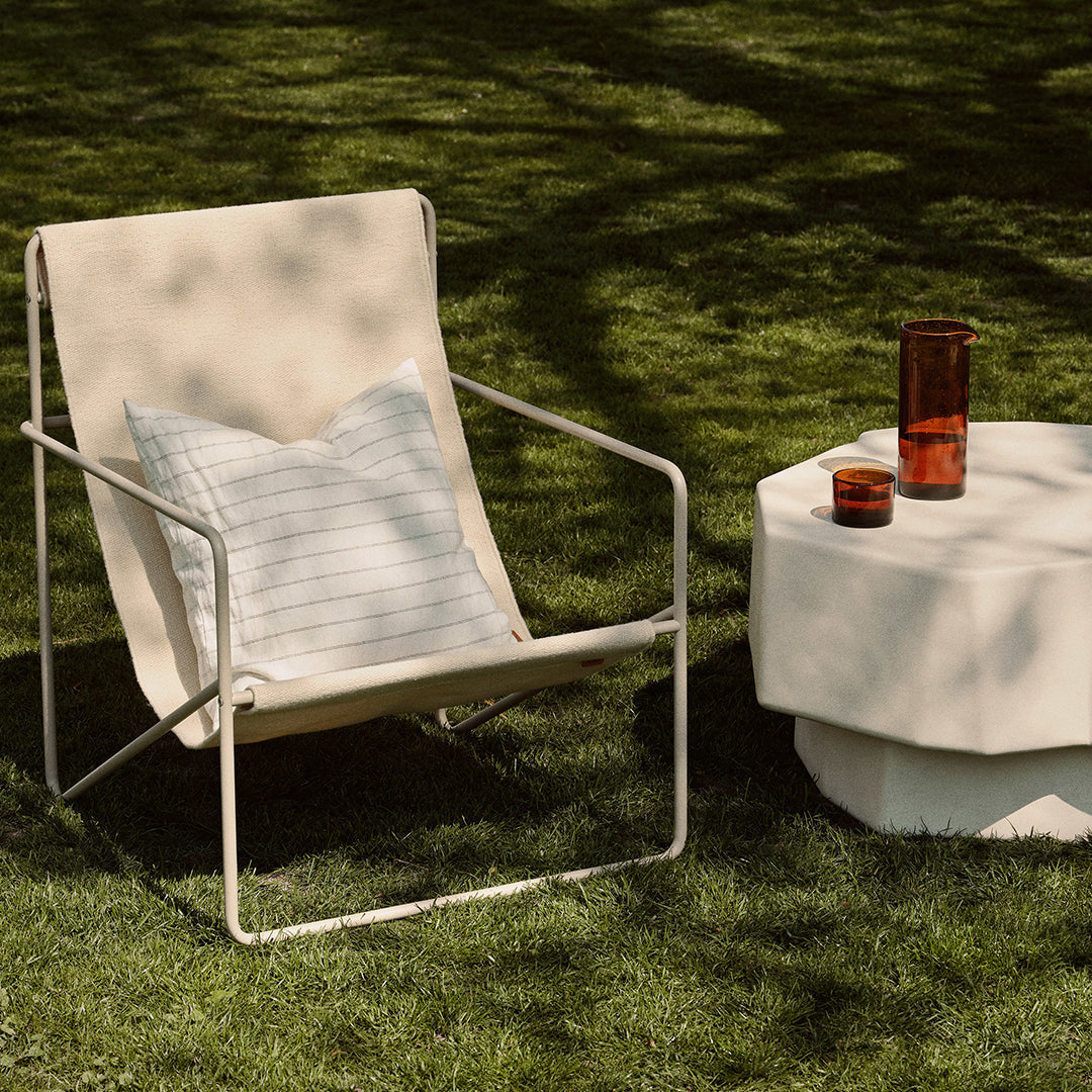 "Beige outdoor chair with a striped pillow beside a white geometric side table and vibrant colored glasses."