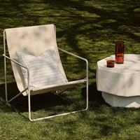 "Beige outdoor chair with a striped pillow beside a white geometric side table and vibrant colored glasses."