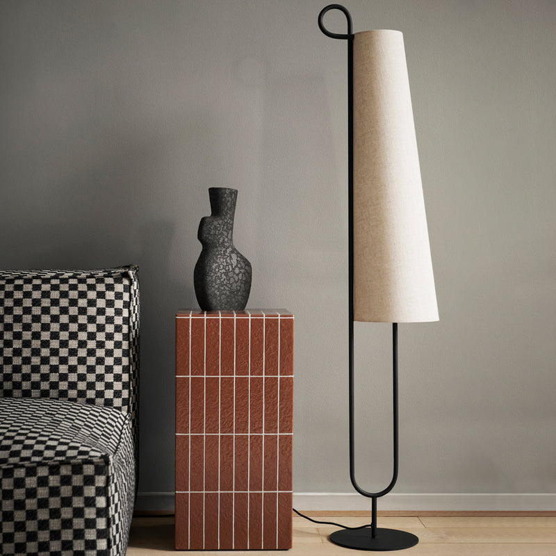 Black and white checkered patterns on sofa, textured black vase, and cream cone-shaped lamp against neutral background.
