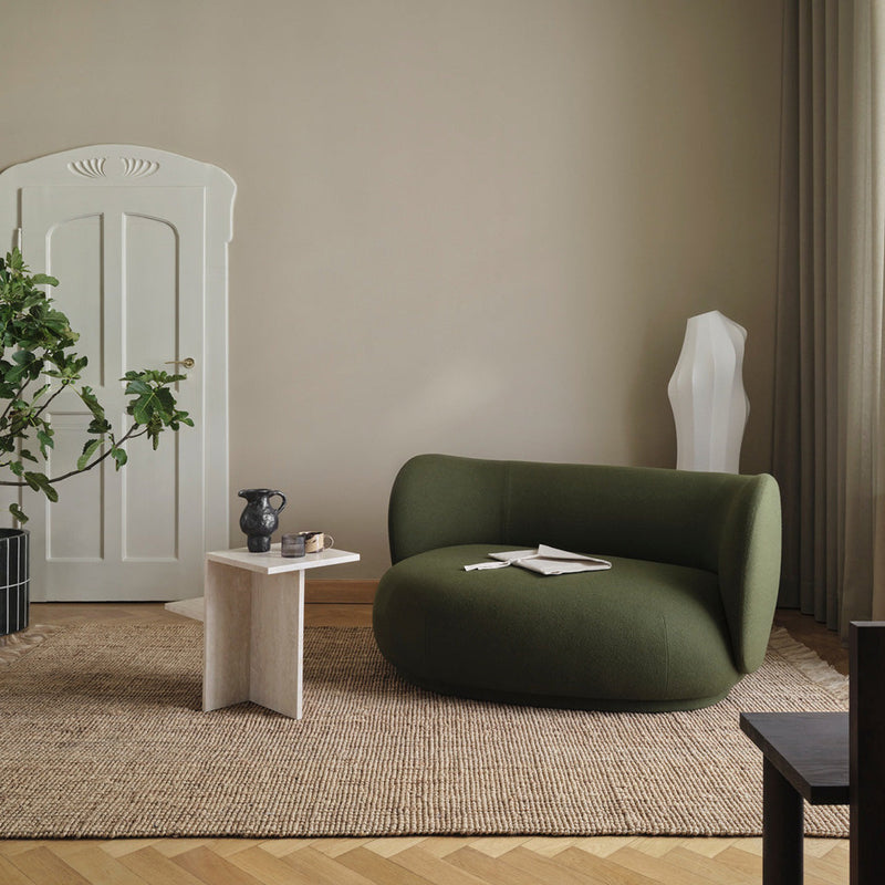 Curved green sofa on a textured beige rug, with neutral walls and a mix of modern decor elements.