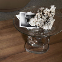 Clear glass bowl with textured white coral and monochrome photographs on a warm wooden surface.