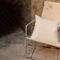 Cream pillow with subtle black stripes on a minimalist lounge chair against a textured stone background.