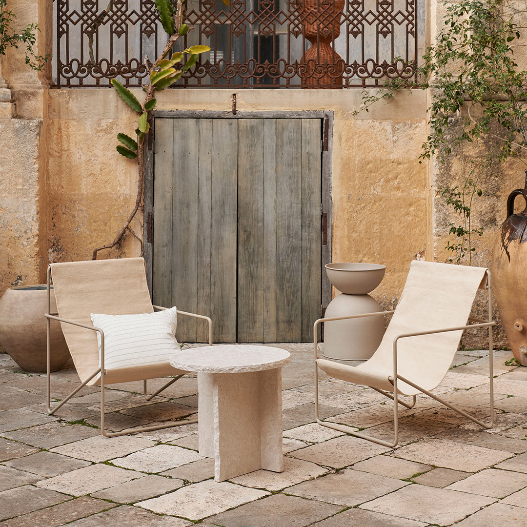 Neutral beige chairs and a textured cream side table against a rustic stone courtyard backdrop.