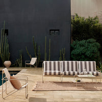 Striped outdoor sofa with gray, cream, and beige patterns, surrounded by greenery on a wooden deck.