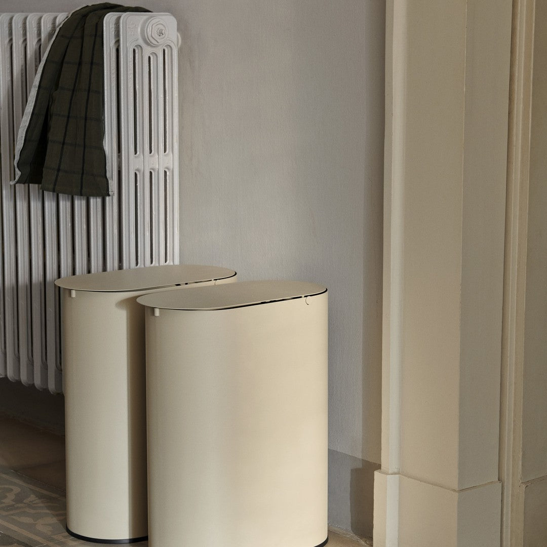 Beige cylindrical storage bins with sleek black trim, set against a soft gray wall and white radiator.