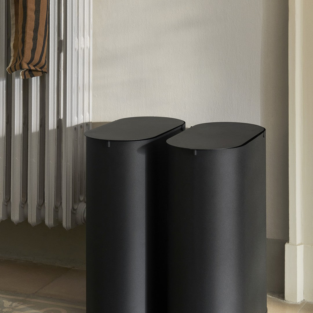 Black cylindrical bins with a sleek matte finish, placed beside a light-colored wall and a striped fabric.