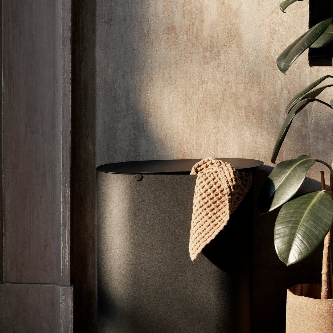 Black cylindrical container with a textured beige towel draped over it, set against a muted, warm-toned background.