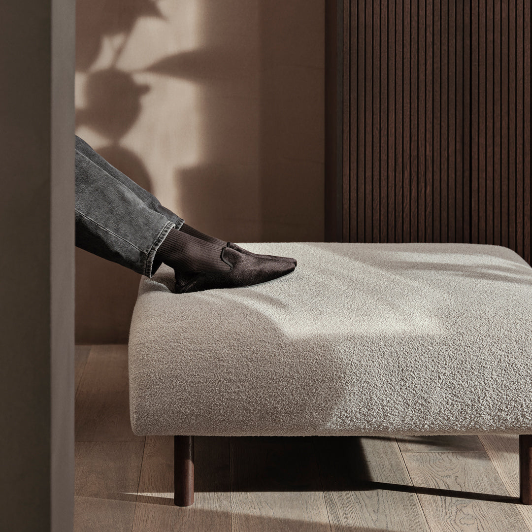 Elevated beige ottoman with a soft texture, featuring dark wood legs and a minimalistic design. Balanced with warm tones.