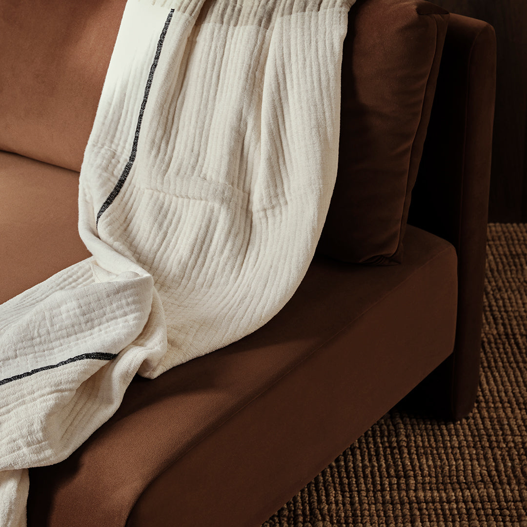 Cream textured blanket with navy stripes draped over a brown sofa, complementing earthy tones.