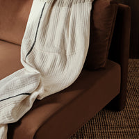Cream textured blanket with navy stripes draped over a brown sofa, complementing earthy tones.