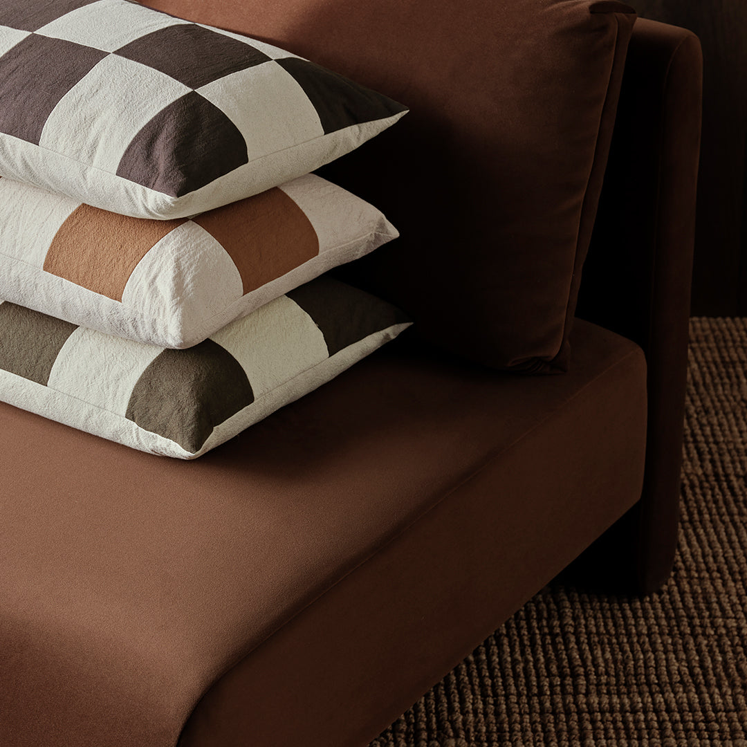 Stylish brown sofa with patterned throw pillows in white, brown, and soft peach hues, perfect for modern décor.