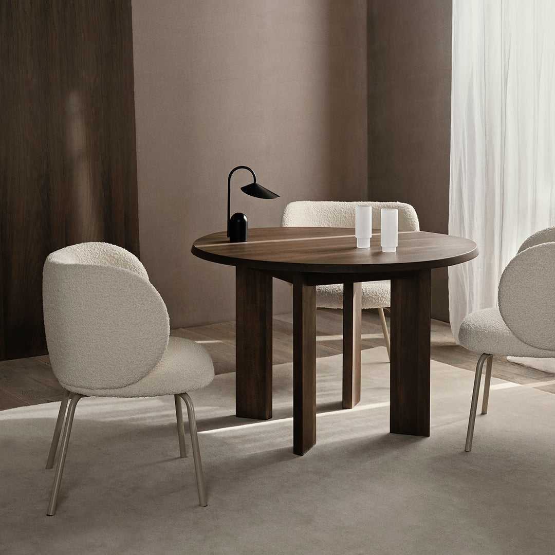 Round wooden table with dark walnut finish, paired with cream upholstered chairs in a minimalist design.