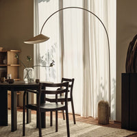 Arched floor lamp with a soft beige shade, sleek black chairs, and beige accents on natural wood tones and light drapes.