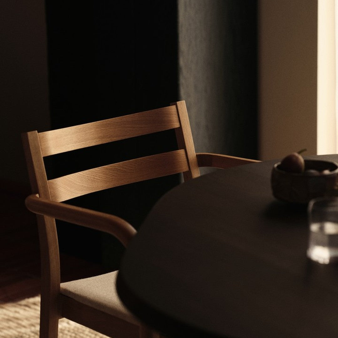 Light wood chair with a minimalist design next to a dark round table, featuring soft neutral tones in a modern setting.