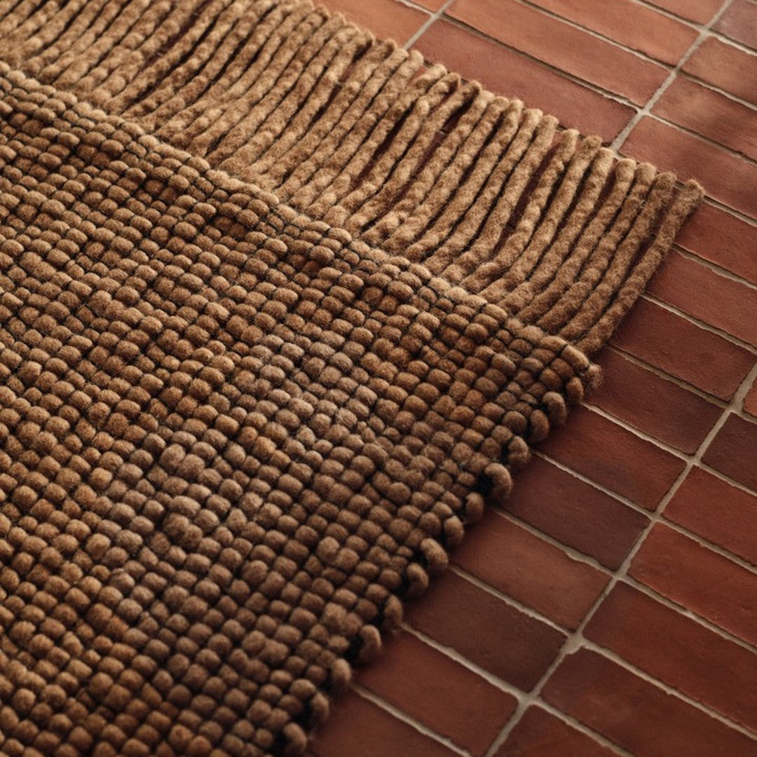 Textured brown rug with chunky patterns and fringed edges, layered over a warm-toned tile surface.