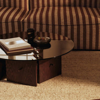 Round black glass coffee table with dark wooden base, set against striped brown and cream sofa and beige rug.