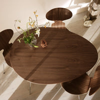 "Round walnut dining table with smooth surface and unique organic shapes, complemented by light wood flooring."