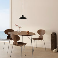 Modern round wooden table with three matching brown chairs, accented by a sleek black pendant light and neutral walls.